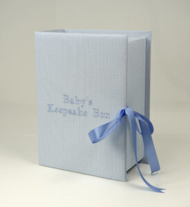 Medium light blue seersucker check keepsake box standing upright with matching blue embroidered ‘Baby’s Keepsake Box’ and blue satin ribbon.